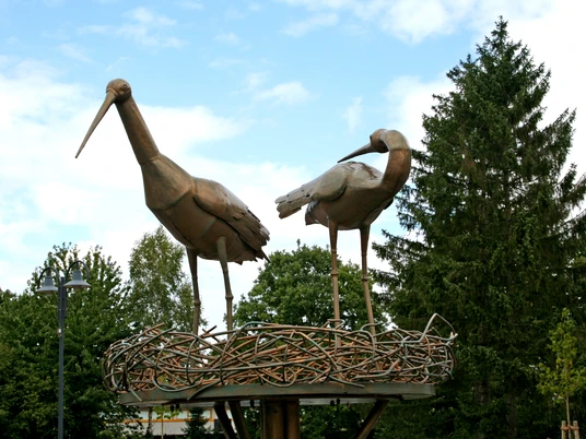 Störche im Kreisel Zwei metallene Storchfiguren stehen auf einem kunstvoll gestalteten Nest inmitten eines Kreisverkehrs.