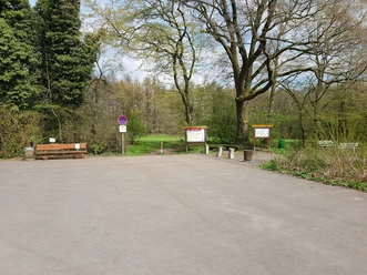 Parkplatz mit Bäumen, Informationstafeln und Sitzbänken am Waldrand, ohne Park- und Halteverbotsschild.