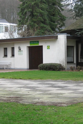 Gästepavillon in der Oldendorfer Schweiz Pavillon in bewaldeter Umgebung mit Schachbrettplatz im Vordergrund, umringt von Bäumen und Gebäuden.