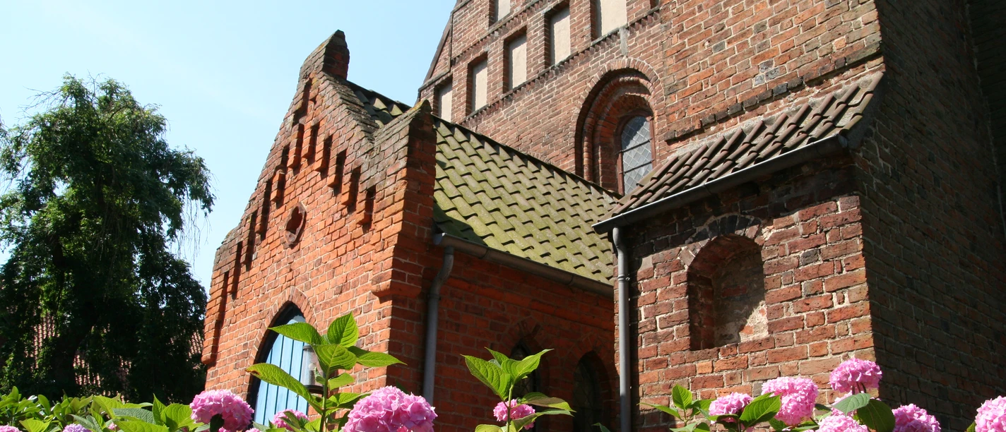 Kirche St. Cosmae und Damiani Backsteinkirche mit hübschen Dachfirsten und Rosen im Vordergrund unter klarem blauem Himmel.