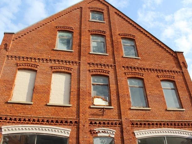 A historic brick building with large windows and decorative brick patterns under a blue sky.