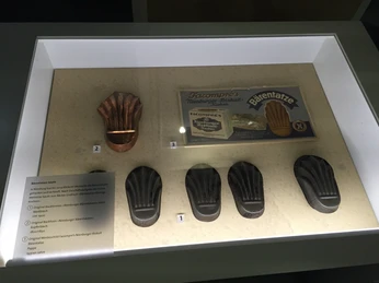 Eine beleuchtete Vitrine zeigt fünf Backformen für Nienburger Bärentatzen, eine traditionelle Süßspeise.