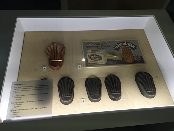 Eine beleuchtete Vitrine zeigt fünf Backformen für Nienburger Bärentatzen, eine traditionelle Süßspeise.