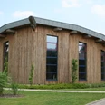 Ein modernes rundes Gebäude mit Holzfassade und markant geneigtem Metalldach, von Natur umgeben.