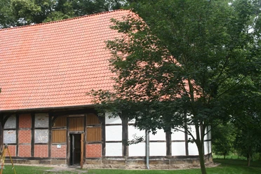 Kloster Schinna Das Bild zeigt ein historisches Fachwerkgebäude mit rotem Ziegeldach, umgeben von grünen Bäumen.