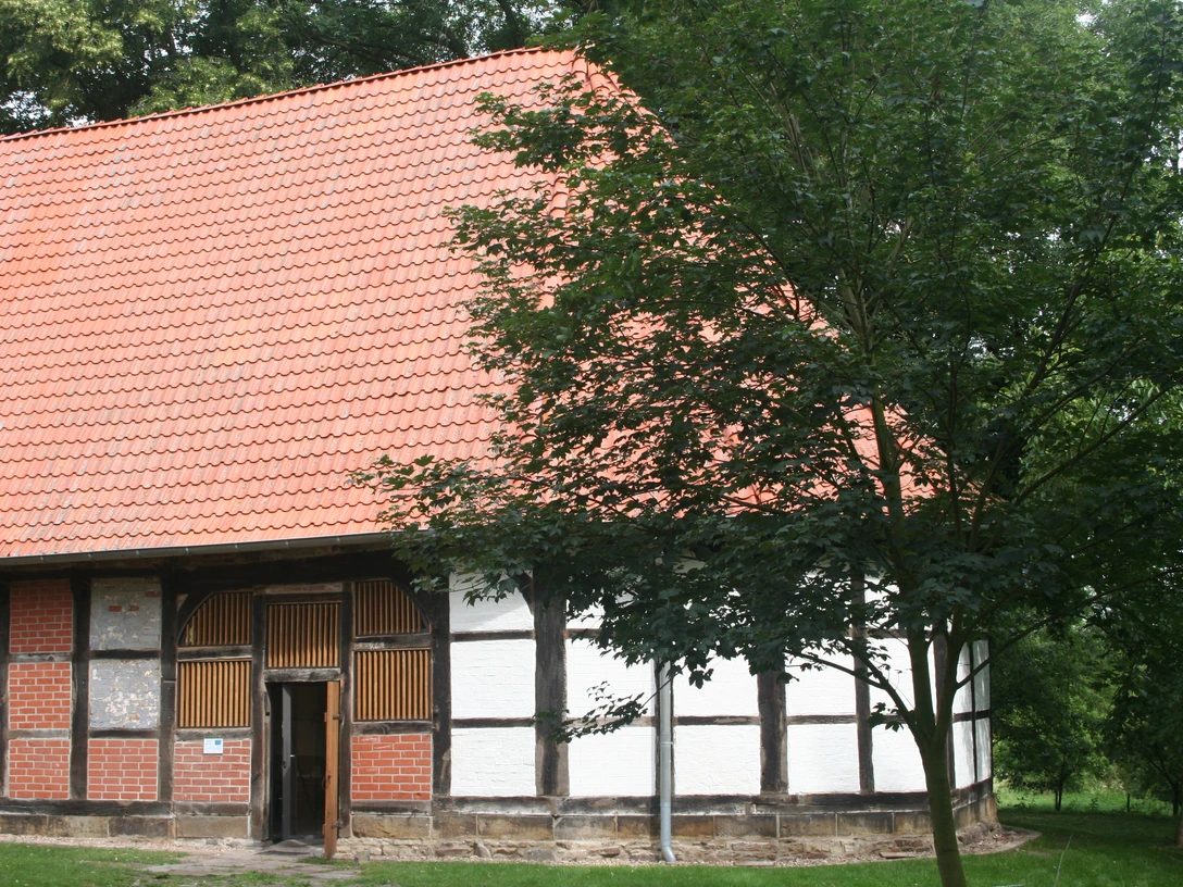 Kloster Schinna Das Bild zeigt ein historisches Fachwerkgebäude mit rotem Ziegeldach, umgeben von grünen Bäumen.