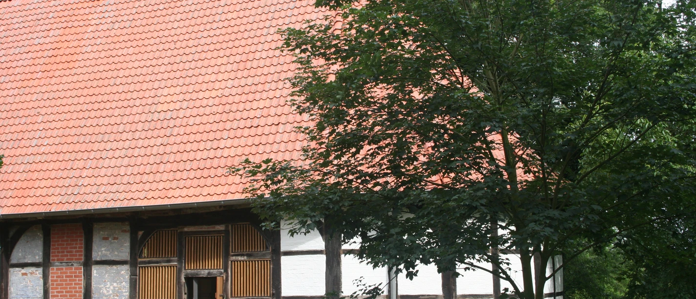 Kloster Schinna Das Bild zeigt ein historisches Fachwerkgebäude mit rotem Ziegeldach, umgeben von grünen Bäumen.