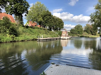 Hafen Stolzenau mit Bootanleger, umgeben von grünen Bäumen, gespiegelt in ruhigem Wasser.