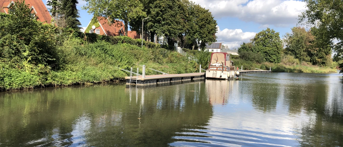 Hafen Stolzenau Hafen Stolzenau mit Bootanleger, umgeben von grünen Bäumen, gespiegelt in ruhigem Wasser.