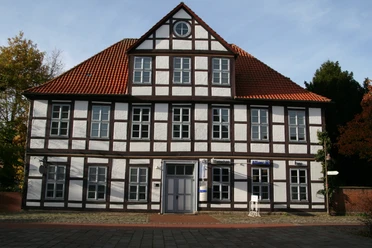 Hakenhof Zweistöckiges Fachwerkhaus mit roten Ziegeldach und symmetrisch angeordneten weißen Fensterreihen.