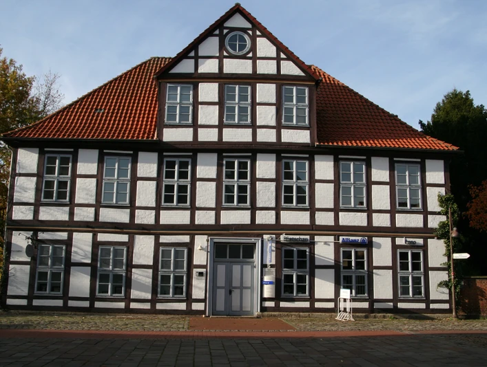 Hakenhof Zweistöckiges Fachwerkhaus mit roten Ziegeldach und symmetrisch angeordneten weißen Fensterreihen.