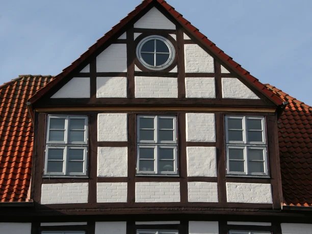 Hakenhof Fachwerkhaus mit roten Ziegeln und einer kleinen, runden Fenster im Giebel unter blauem Himmel.
