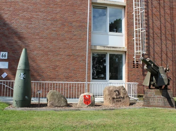 Ausstellungsstück einer militärhistorischen Sammlung, bestehend aus Geschütz, Munitionshülse und Gedenksteinen.