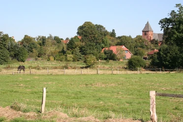 St.-Sigismund-Kirche in Daverden Grüne Wiesen mit Pferd vor der St.-Sigismund-Kirche in Daverden, umgeben von Bäumen und Gebäuden.