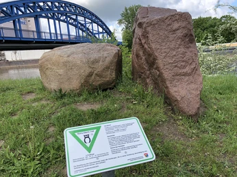 Findling Zwei große Findlinge stehen auf einer Wiese, im Hintergrund ist eine blaue Brücke zu sehen.