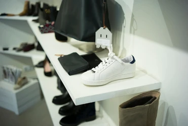 THE WANTS SHOES Weißer Sneaker auf einem Display, umgeben von verschiedenen Accessoires und Schuhen in neutralen Tönen.