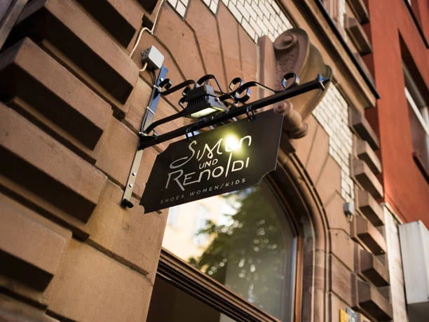 Simon und Renoldi Ein elegantes Schild mit der Aufschrift „Simon und Renoldi“ hängt an einer architektonisch verzierten Hausfassade.