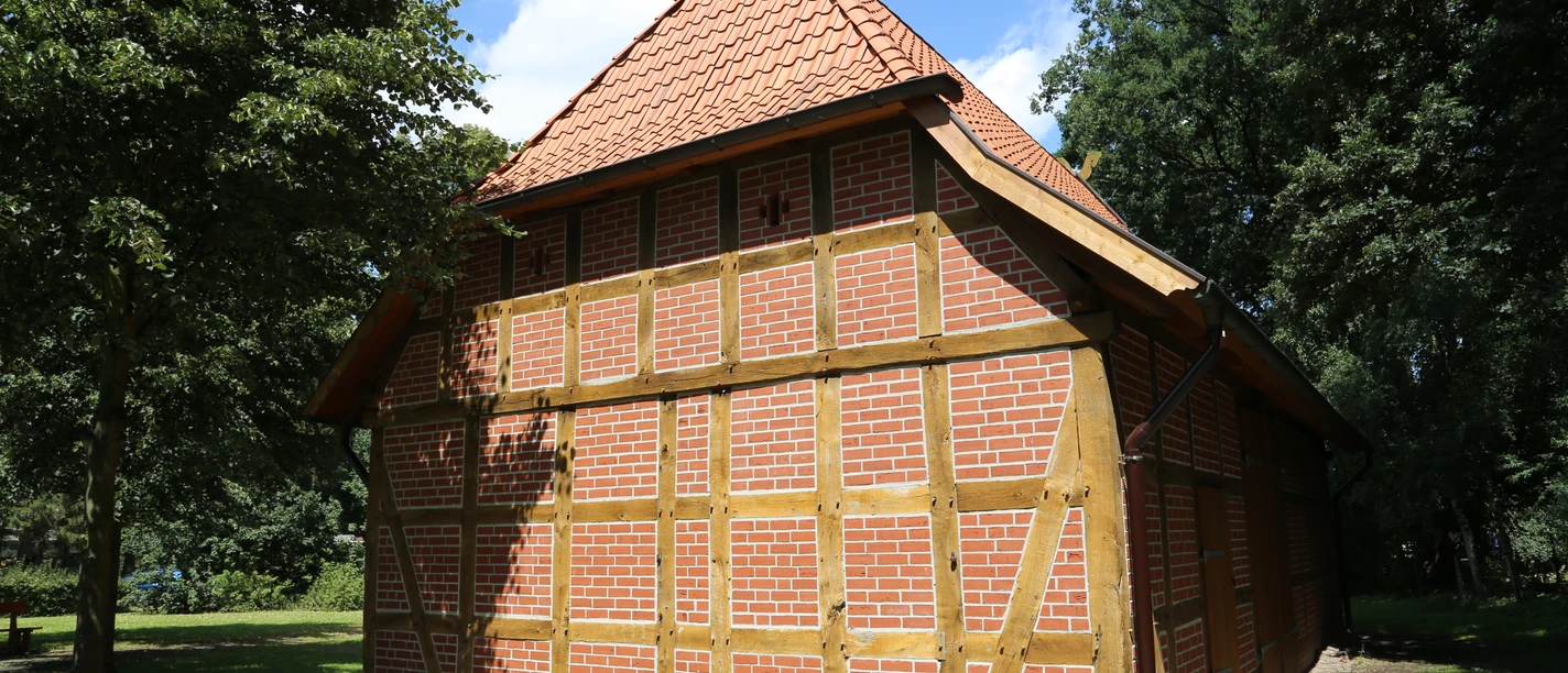 Ein traditionelles Fachwerkgebäude mit rotem Ziegeldach im Grünen bei sonnigem Wetter.