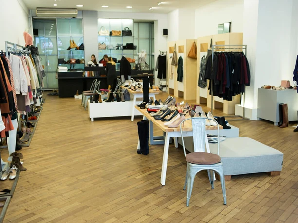 PREGO The image shows a modern store with stylish clothing, accessories and shoes neatly displayed on wooden shelves and tables. The salesroom is brightly lit, with clean lines and a welcoming atmosphere.
