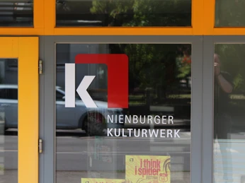 Nienburger Kulturwerk Nienburger Kulturwerk mit auffälligem Logo an der Glasfassade, im Hintergrund parkende Autos.