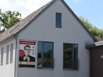 Ein modernes Gebäude mit klassischen Zügen, helle Fassade, große Fenster und ein Plakat an der Wand.