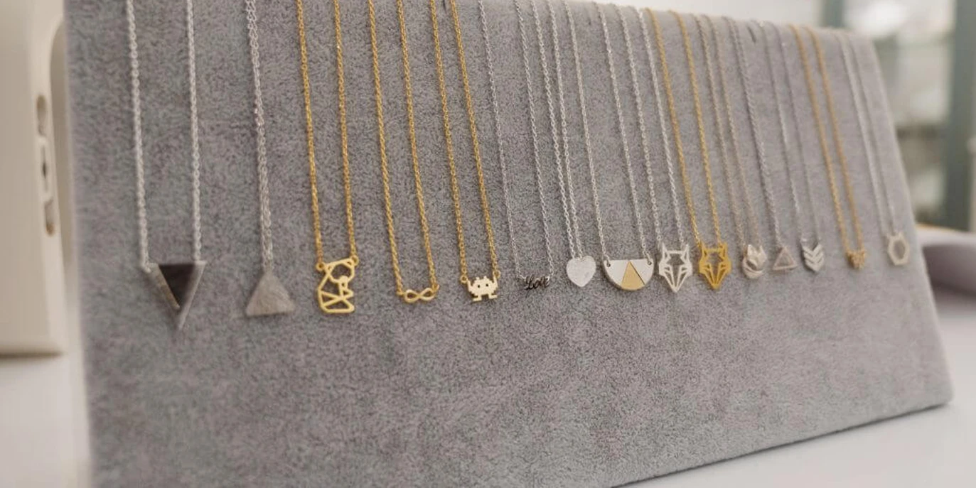 APRICOT room Eine Auswahl zarter Halsketten mit unterschiedlichen Anhängern hängt auf einer grauen Präsentationsfläche.A selection of delicate necklaces with different pendants hangs on a gray display area.