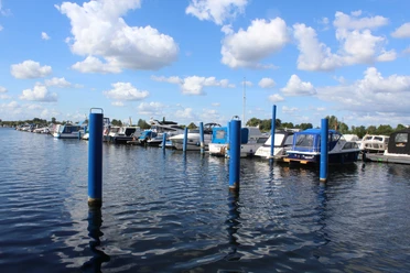 Wieltsee Weyhe Boote liegen am Steg eines Sees unter blauem Himmel. Die Wasseroberfläche wellt sich leicht im Wind.