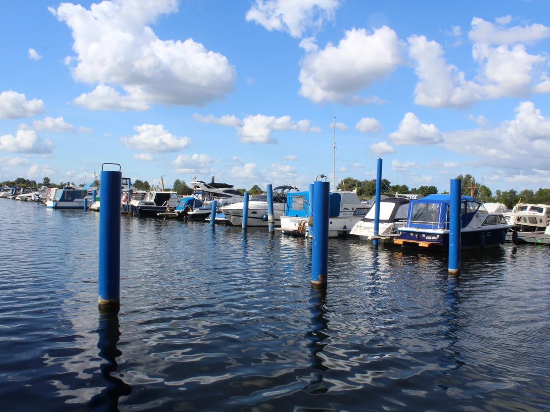 Wieltsee Weyhe Boote liegen am Steg eines Sees unter blauem Himmel. Die Wasseroberfläche wellt sich leicht im Wind.