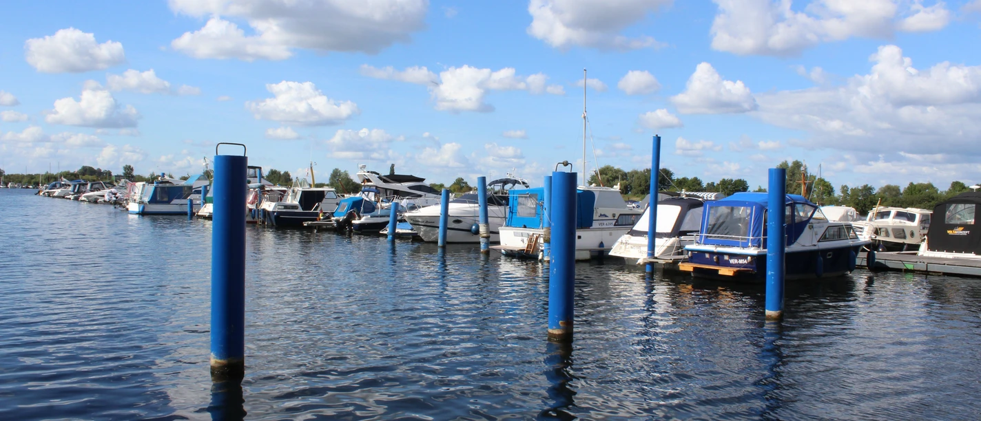 Wieltsee Weyhe Boote liegen am Steg eines Sees unter blauem Himmel. Die Wasseroberfläche wellt sich leicht im Wind.