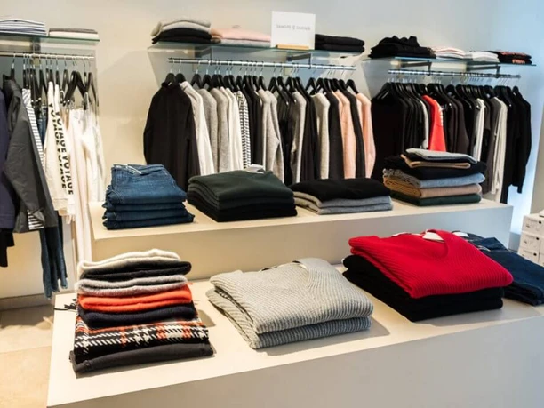 Style the brandstore A stylishly furnished boutique with piles of sweaters in different colors on a table and neatly hung clothes in the background.