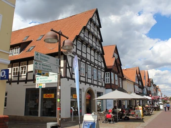 Fachwerkhaus mit rotem Dach in Nienburg, umgeben von Geschäften und Straßencafés bei bewölktem Himmel.