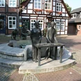 Spargelbrunnen Skulptur eines Spargelbauern mit Tafel und zwei weiteren Figuren vor historischen Fachwerkhäusern.