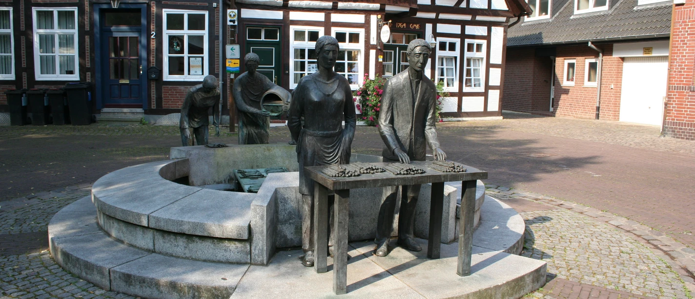 Spargelbrunnen Sculpture of an asparagus farmer with a table and two other figures in front of historic half-timbered houses.