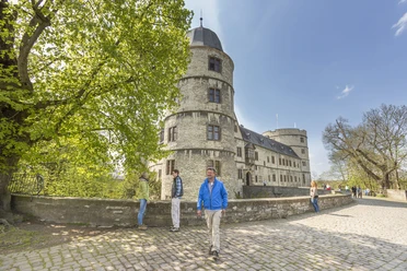 Wanderer an der Wewelsburg Auf einem gepflasterten Weg steht ein Wanderer vor der dreistöckigen, runden Wewelsburg.
