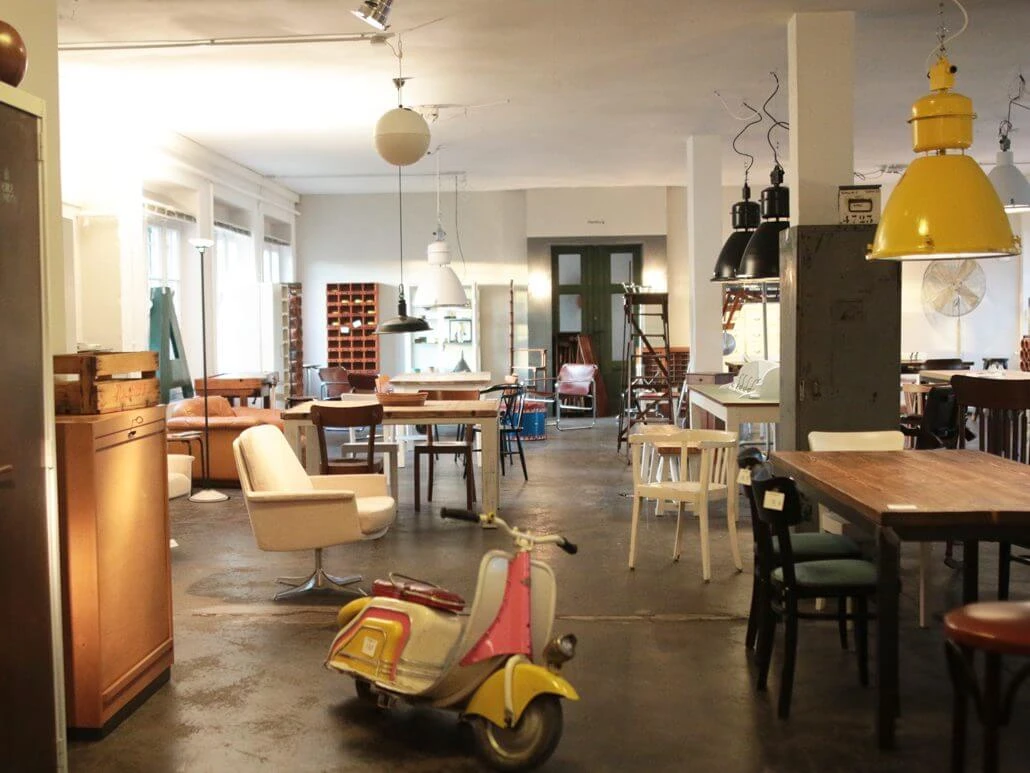 Geliebte Möbel Ein gemütlicher Vintage-Möbelladen mit buntem Roller, stilvollen Leuchten und Holzmöbeln.A cozy vintage furniture store with colorful scooters, stylish lamps and wooden furniture.
