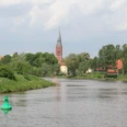 Weser bei Nienburg Die Weser schlängelt sich durch eine grüne Landschaft bei Nienburg; ein Kirchturm ragt im Hintergrund empor.