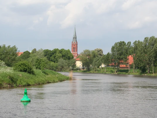 Weser bei Nienburg Die Weser schlängelt sich durch eine grüne Landschaft bei Nienburg; ein Kirchturm ragt im Hintergrund empor.