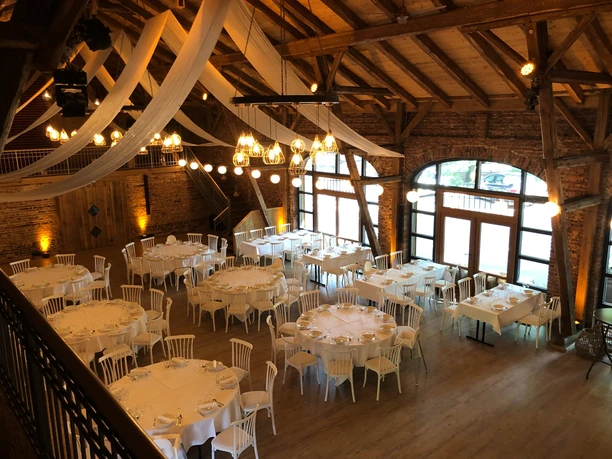 Hof Frien Festsaal Großer, eleganter Festsaal mit Holzbalken, runden und rechteckigen Tischen und dezentem Licht.