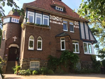 Pilgerherberge Altes Pfarrhaus Historisches Pfarrhaus aus Backstein mit Erker, Türmchen und blumengeschmückten Rundbogenfenstern.Historic brick rectory with bay windows, turrets and arched windows decorated with flowers.Historisk præstegård i mursten med karnapper, tårne og buede vinduer dekoreret med blomster.Historische bakstenen pastorie met erkers, torentjes en boogramen versierd met bloemen.