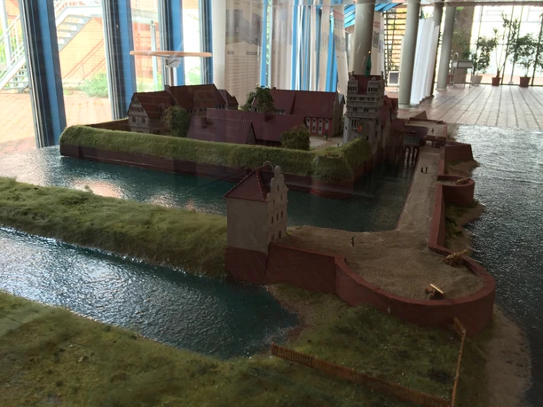 Schlossmodell im Rathaus Nienburg Ein detailliertes Modell eines historischen Schlosses auf einer Insel, umgeben von Wasser und Vegetation.