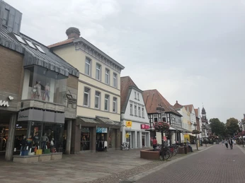 Geschäftsstraße mit historischen Gebäuden und Geschäften in Nienburg, unter grauem Himmel.