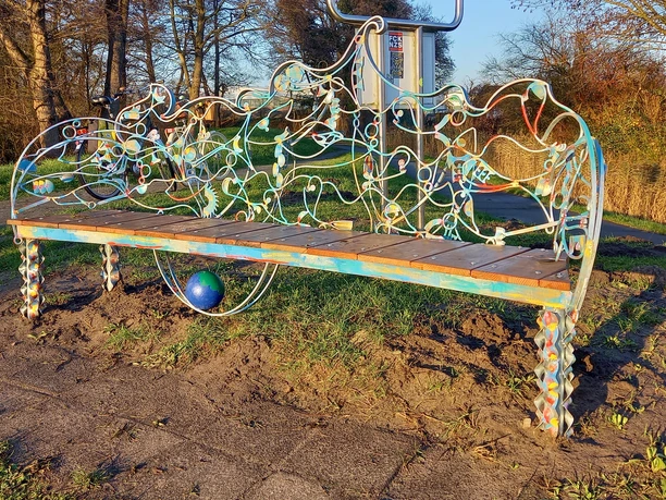 Lieblingsort mit Fischbank Eine kunstvoll geschwungene Metallbank steht in herbstlicher Umgebung, Sonnenlicht betont die filigranen Details.