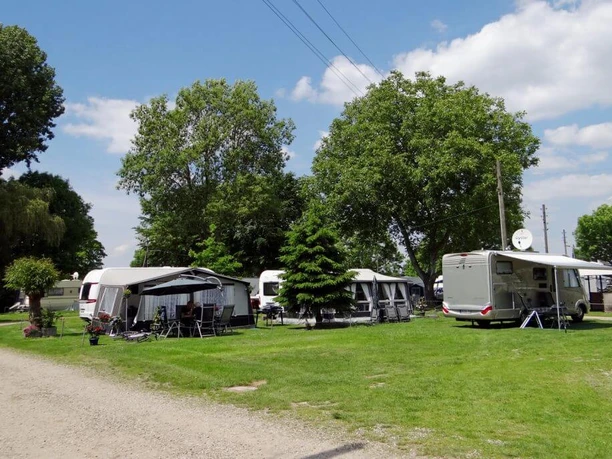 Camping Berger Sorgfältig gepflegte Campingwiese mit Wohnwagen unter Bäumen und strahlend blauem Himmel bei Camping Berger.