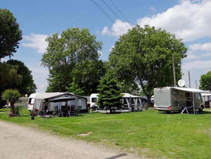 Camping Berger Sorgfältig gepflegte Campingwiese mit Wohnwagen unter Bäumen und strahlend blauem Himmel bei Camping Berger.Carefully maintained camping meadow with caravans under trees and a bright blue sky at Camping Berger.