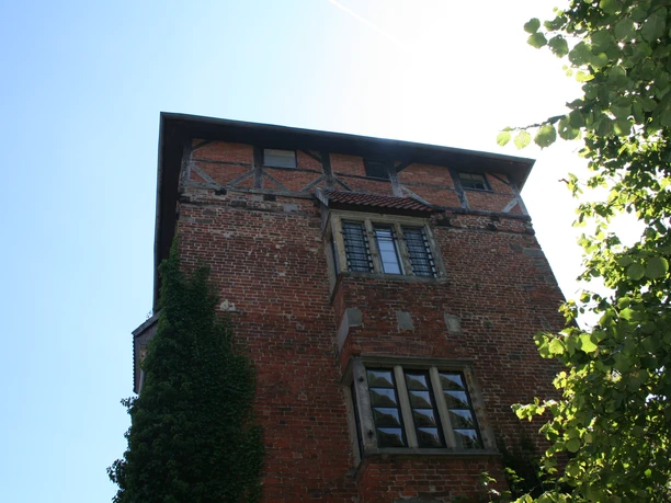 A red brick tower in Nienburg with historic half-timbered elements and surrounding vegetation.