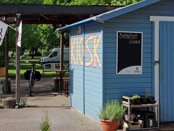 Campsite City of Cologne A blue kiosk on a campsite with signs for "Garden Café" and "Breakfast Service".