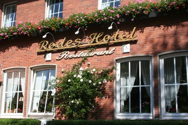 Rodes Hotel Rotes Backsteingebäude mit Blumen geschmückt, darunter der Schriftzug "Rodes Hotel Restaurant".
