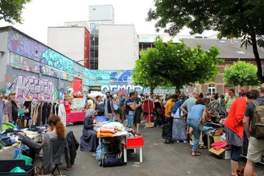 Flohmarkt an der Alten Feuerwache Besucher stöbern auf einem belebten Flohmarkt im Freien, umgeben von Streetart und Gebäuden.