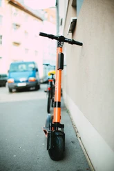 pexels-markus-spiske-3671151.jpg Ein oranges Elektromoped steht auf einem Gehweg, angelehnt an eine Hauswand in einer städtischen Umgebung.