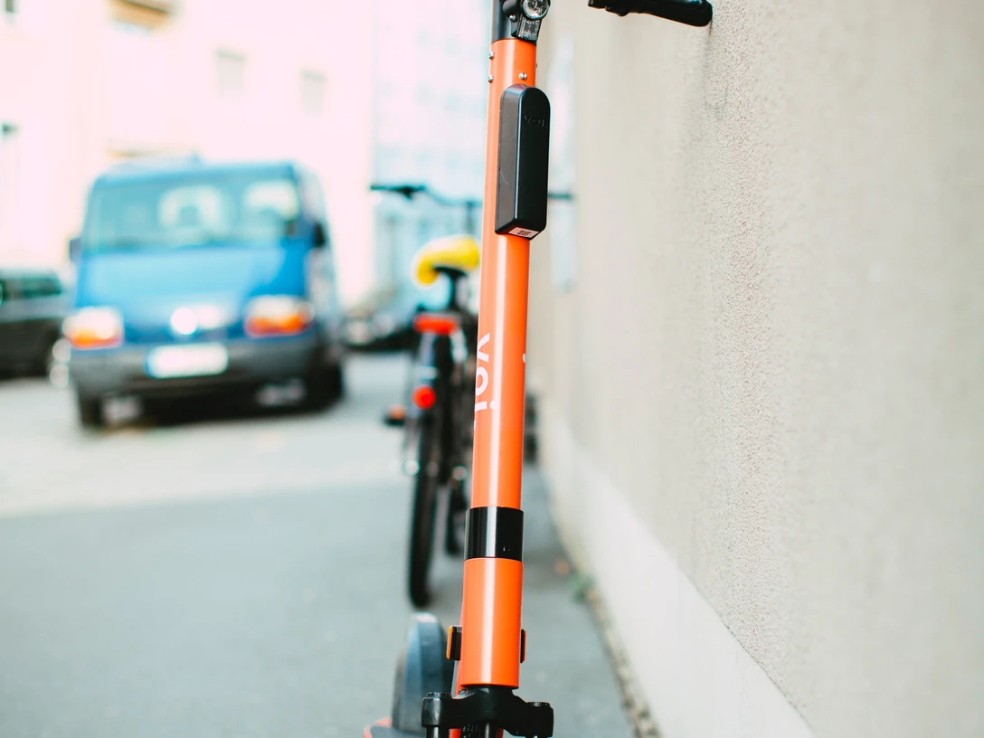 pexels-markus-spiske-3671151.jpg Ein oranges Elektromoped steht auf einem Gehweg, angelehnt an eine Hauswand in einer städtischen Umgebung.